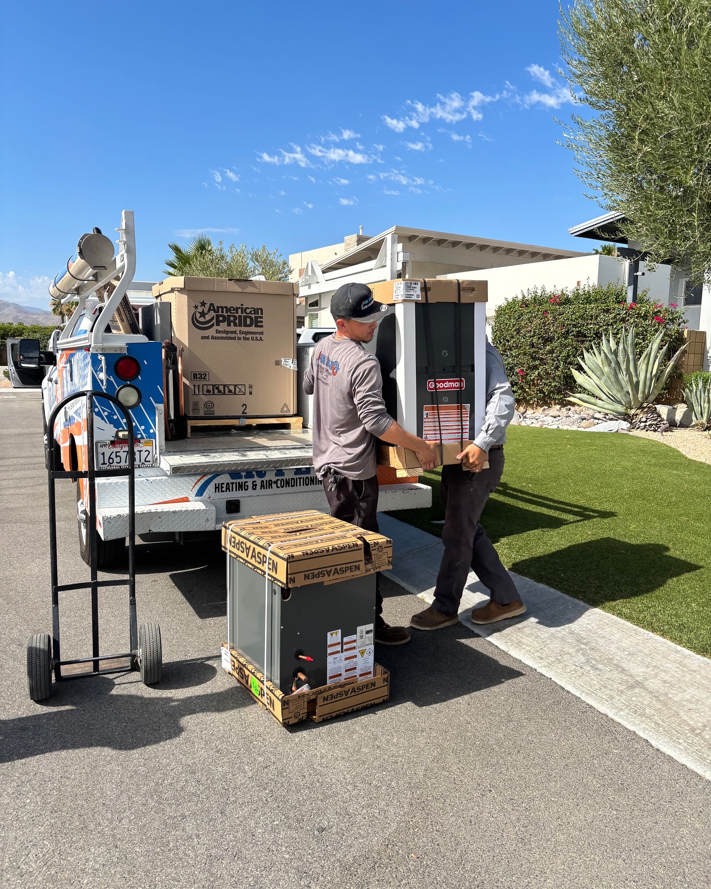Air Plus installers carrying a new Goodman condenser to a customer home