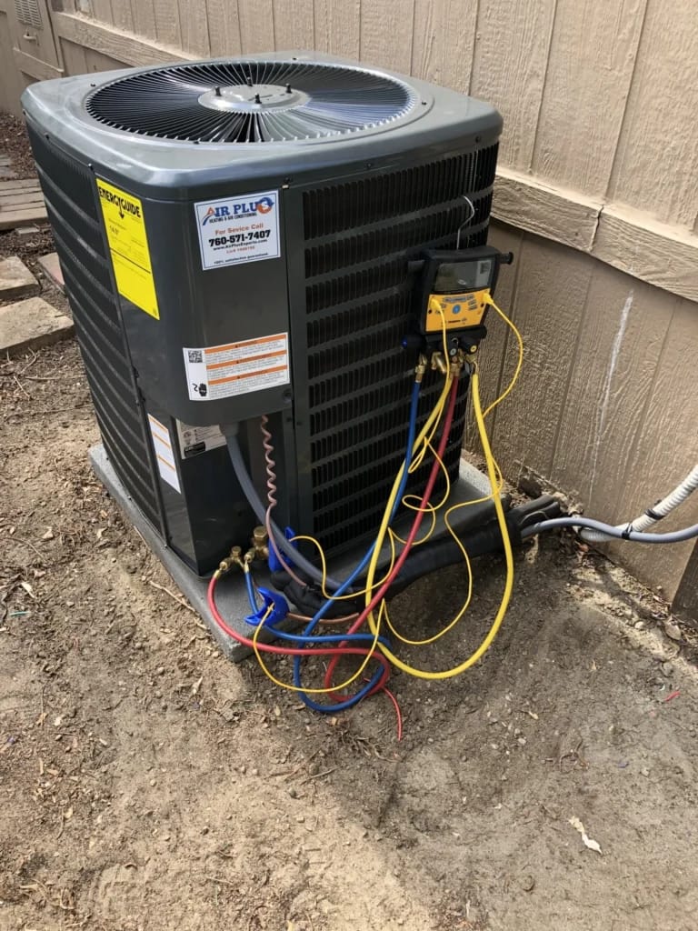 Outdoor HVAC air conditioner condenser unit undergoing professional maintenance and diagnostic testing with digital manifold gauges.