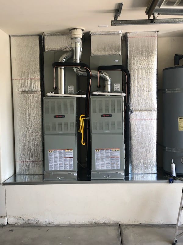 Dual Trane gas furnace and HVAC units installed side-by-side with insulated ductwork and venting in a residential garage setting.
