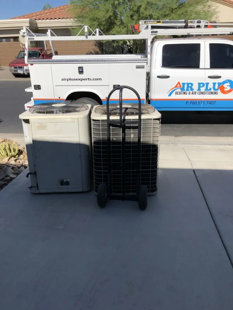 An aging air conditioning unit staged next to its high-efficiency replacement beside an Air Plus service truck during a system changeout.