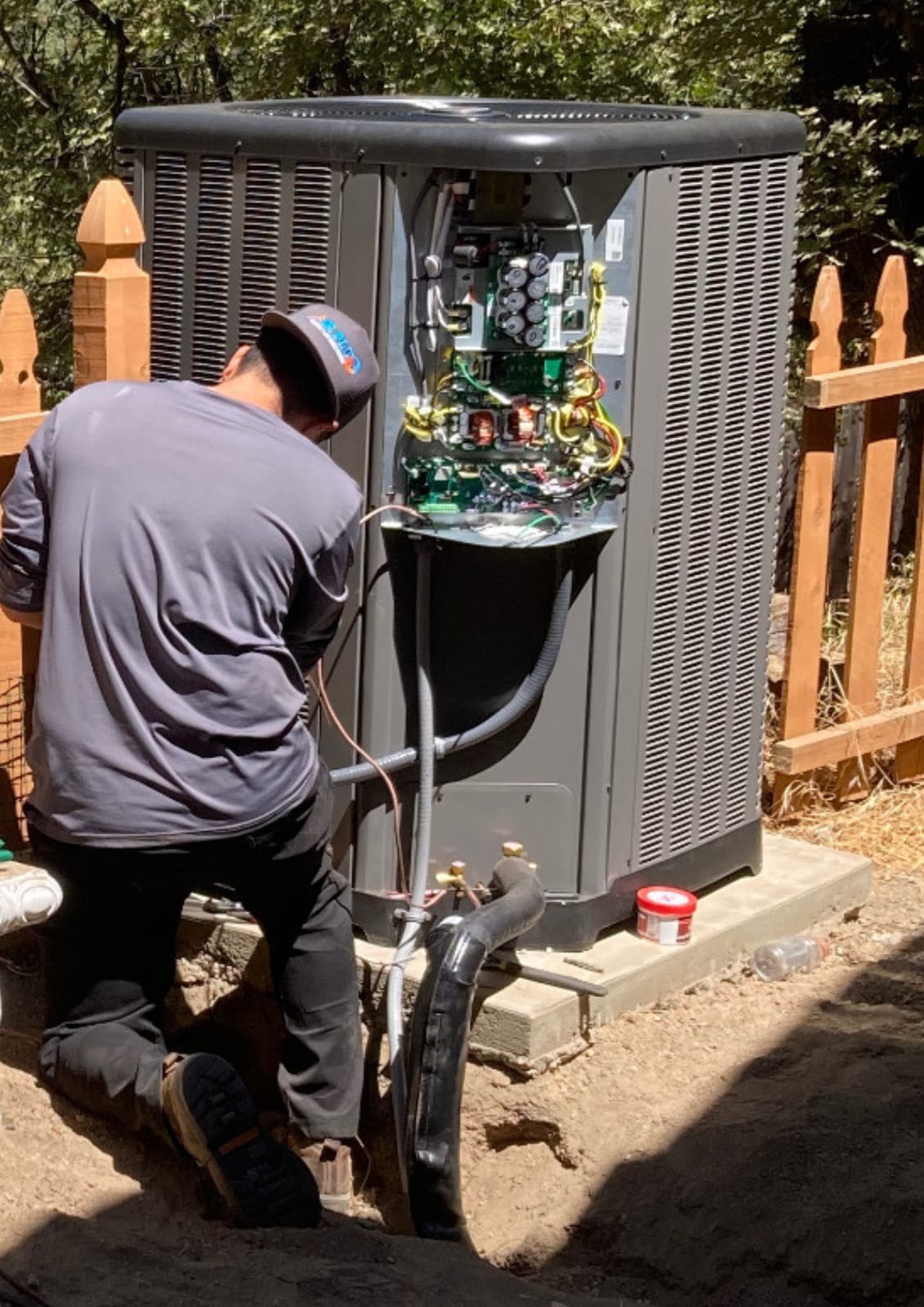 Air Plus technician servicing the internal electrical components of an outdoor condenser during a seasonal maintenance visit.
